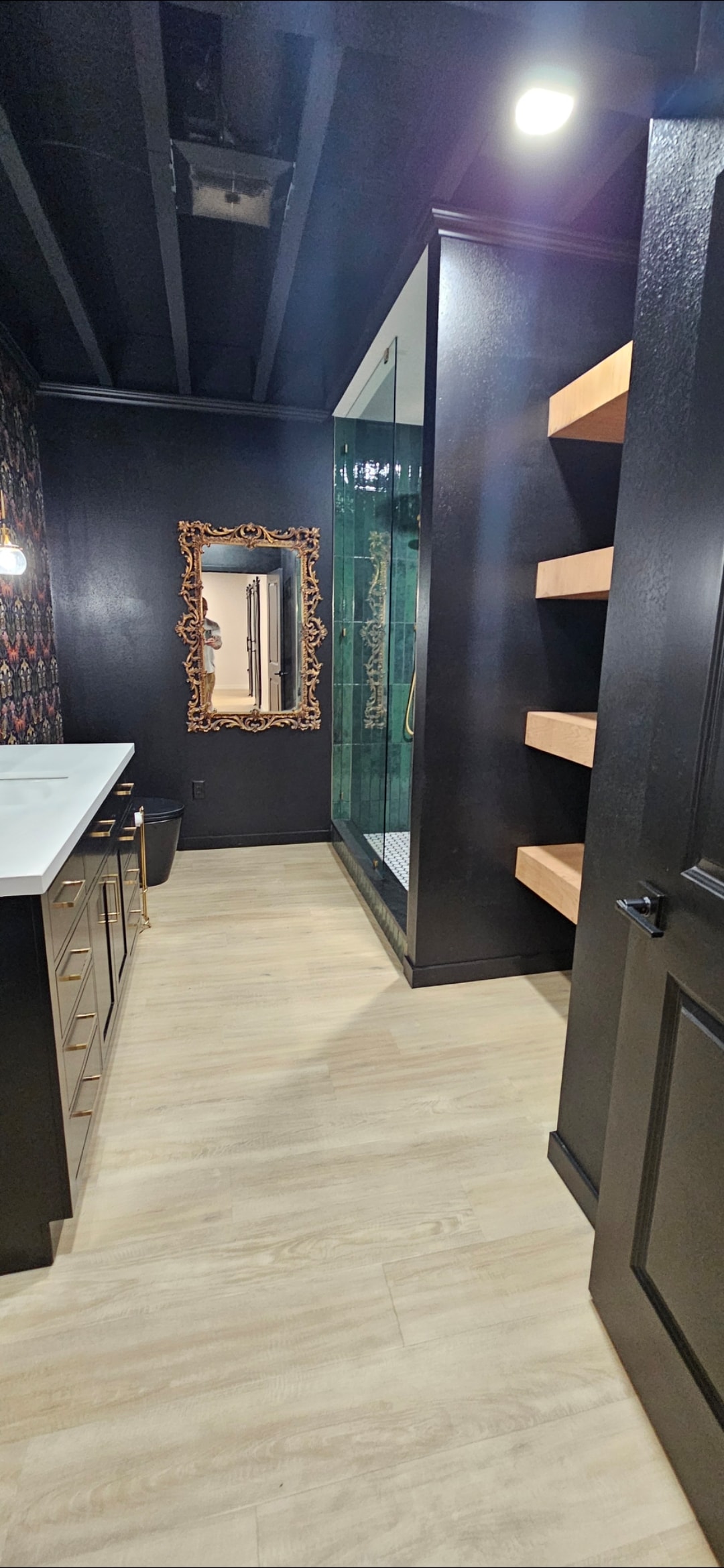 Finished bathroom entrance with shower, floating wood shelves and black finishes.