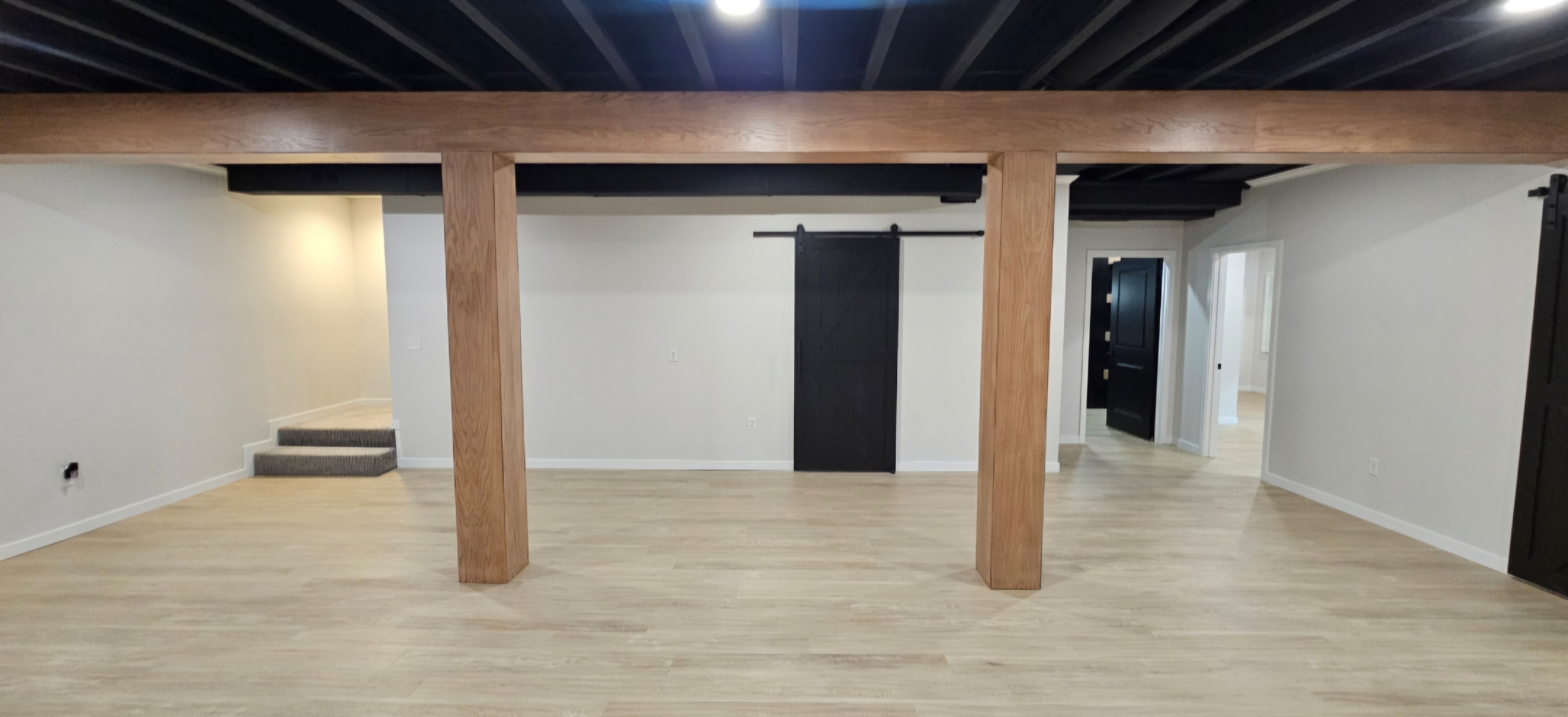 Finished basement straight-on view with wrapped structural beams and a black barn door.