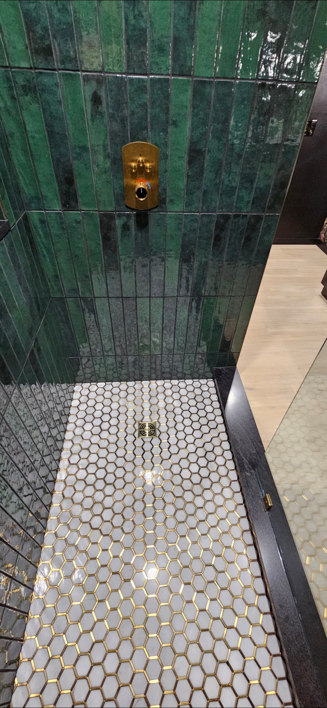 Shower-floor detail with hexagonal mosaic tile, brass accents and linear threshold.